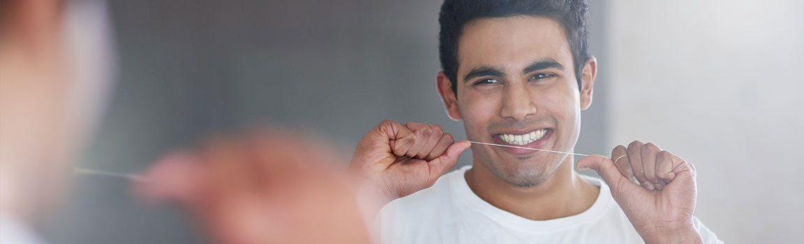 A man is flossing his teeth in front of a mirror