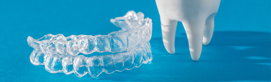 A clear mouth guard and a model of a tooth are on a blue surface
