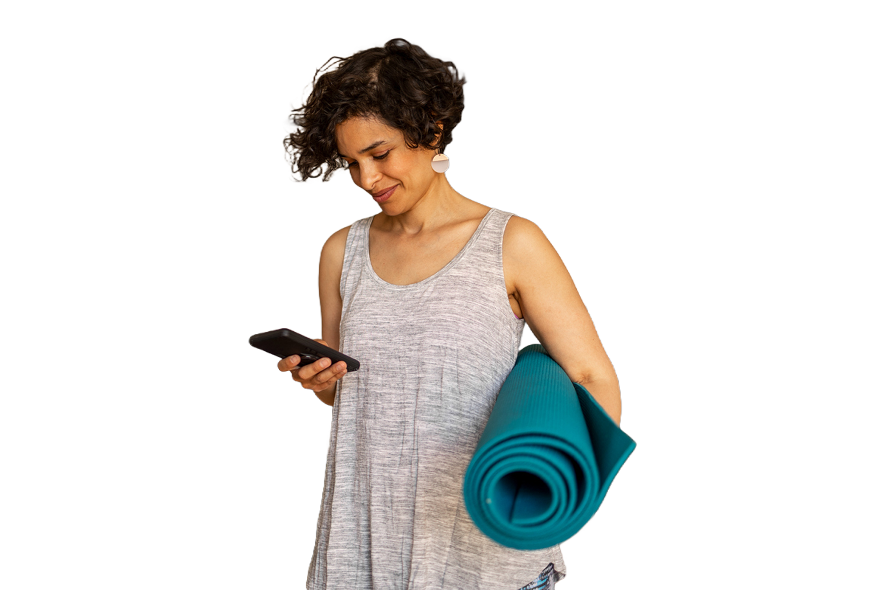 A woman with short brown hair, in a grey tank top, looking at her phone, while holding a yoga mat.